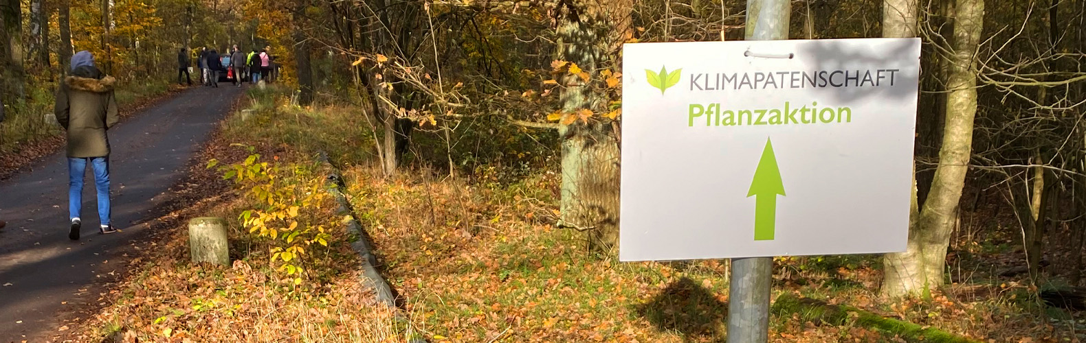 Waldweg mit Laub und ein Schild mit der Aufschrift "Klimapatenschaft Pflanzaktion"